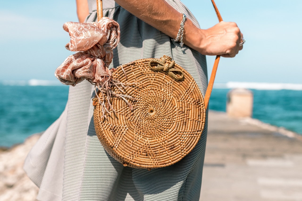 A woman with a circular purse at the beach wears two white gold chain bracelets.