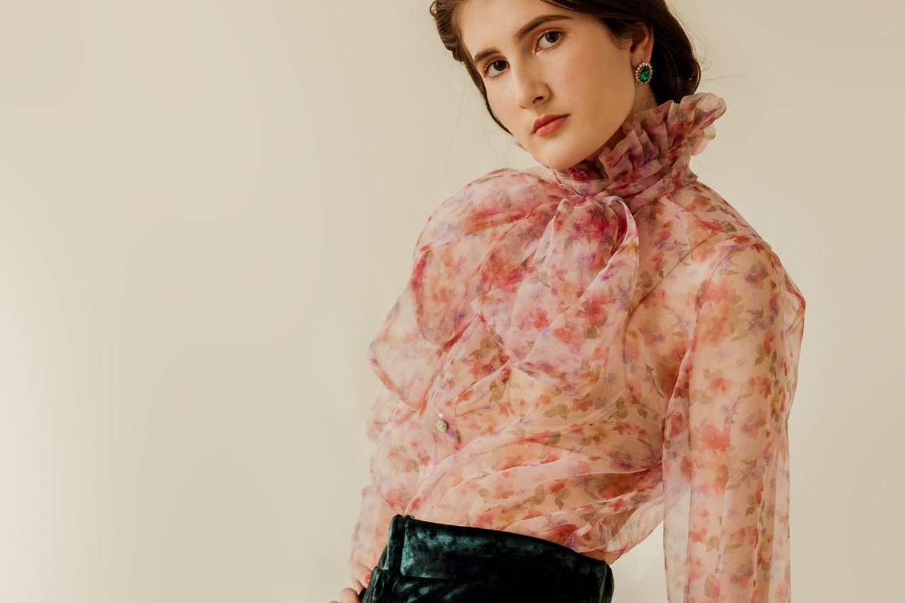 a woman wearing a floral blouse and a bold pair of emerald stud earrings