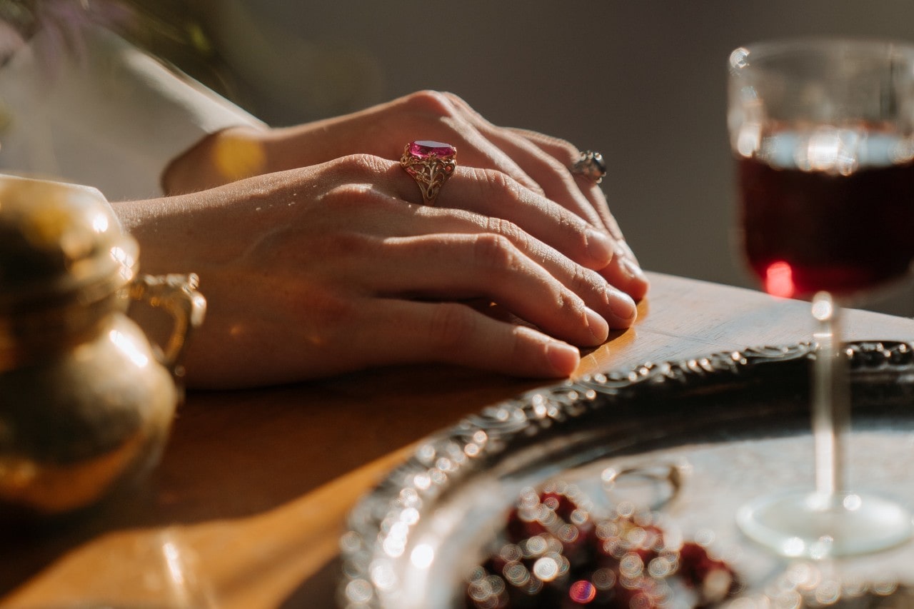 a woman’s hands resting on a set table, donning bold gemstone rings