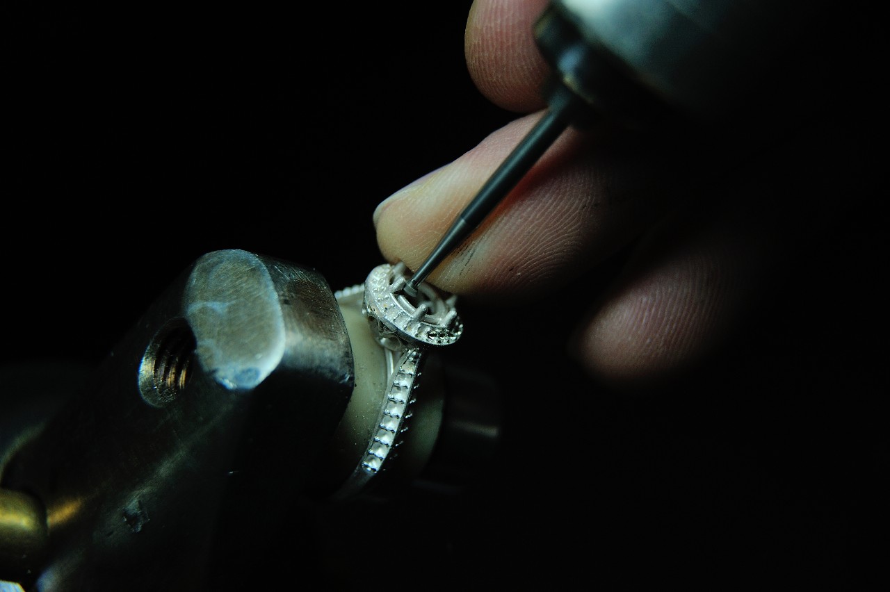 A close-up of a jeweler’s hand as he creates a white gold halo ring with diamonds along the band.