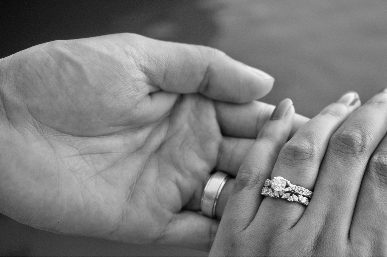A black and white close-up of a bride’s hand in her groom’s, both wearing elegant rings.