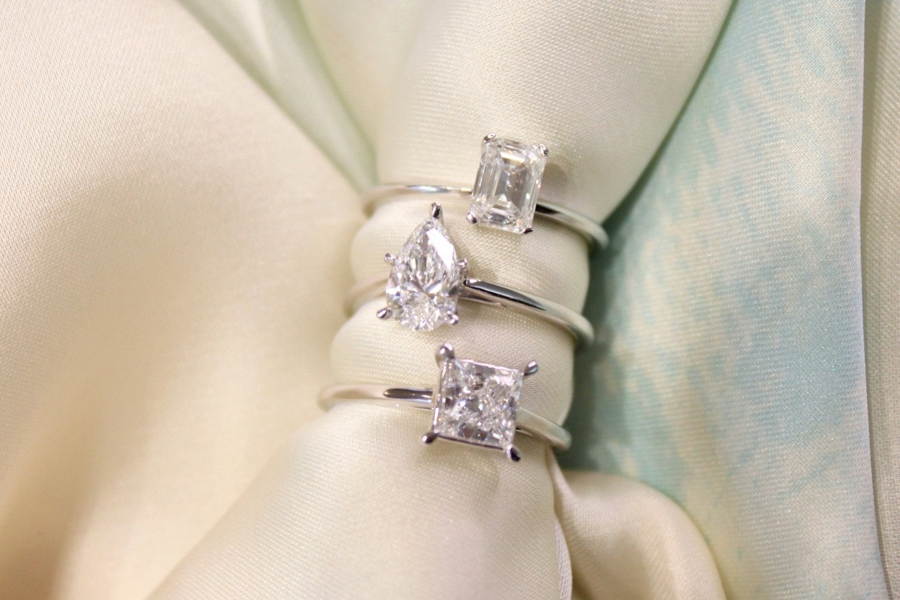 Three white gold solitaire diamond engagement rings stacked together on a piece of fabric.