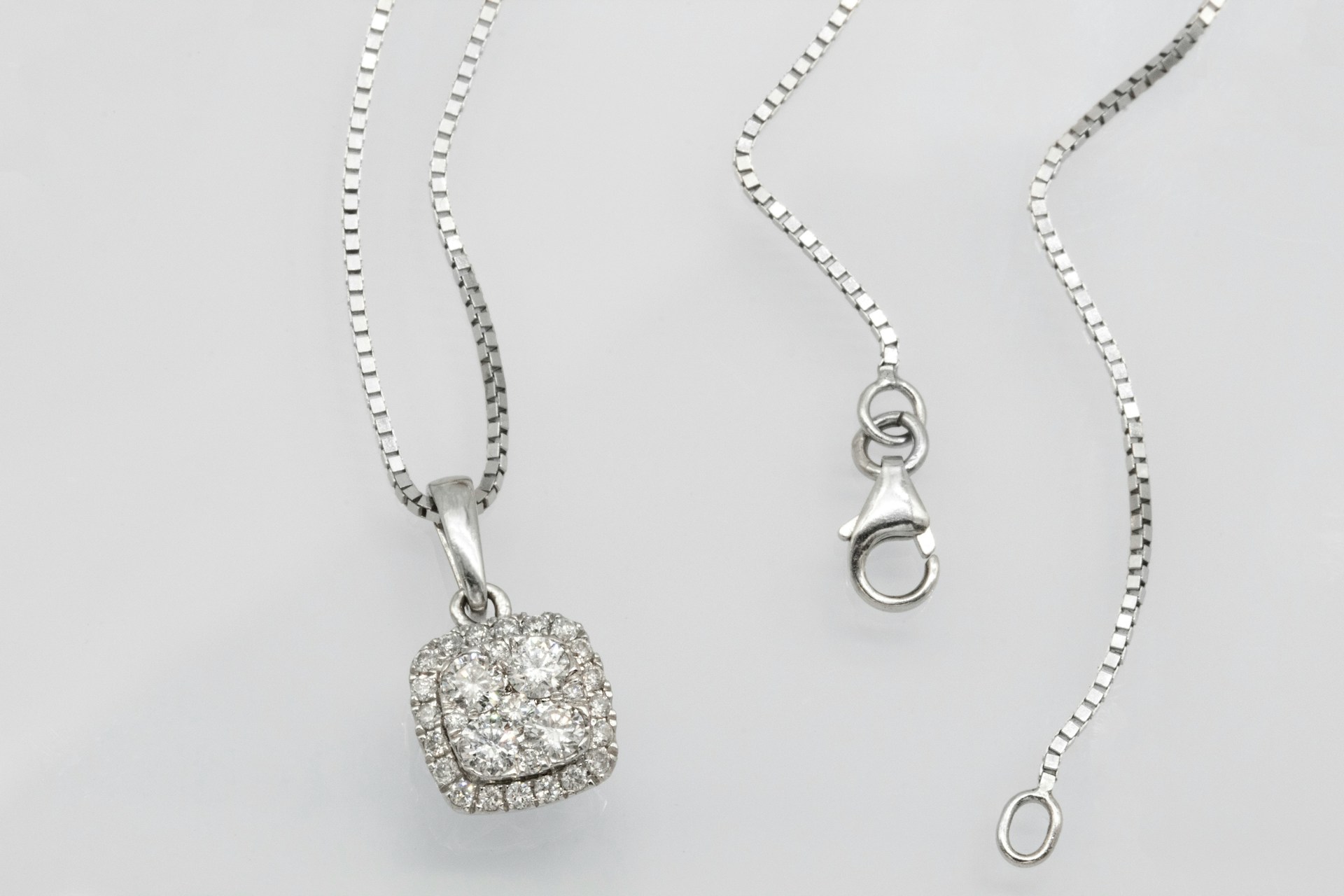 a white gold diamond pendant necklace on a plain gray surface