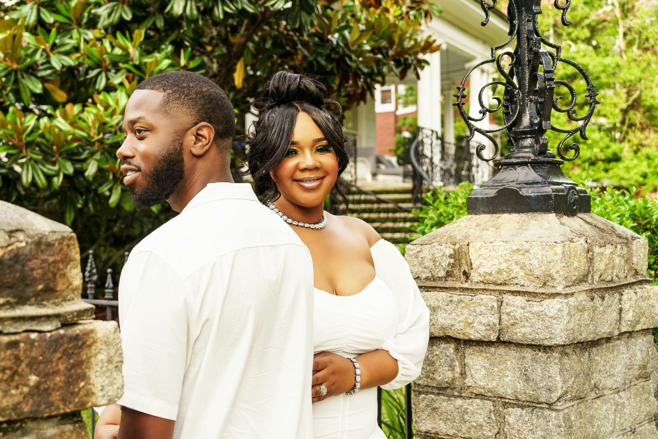 A smiling couple poses outside, standing near a stone pillar and ornate lantern.