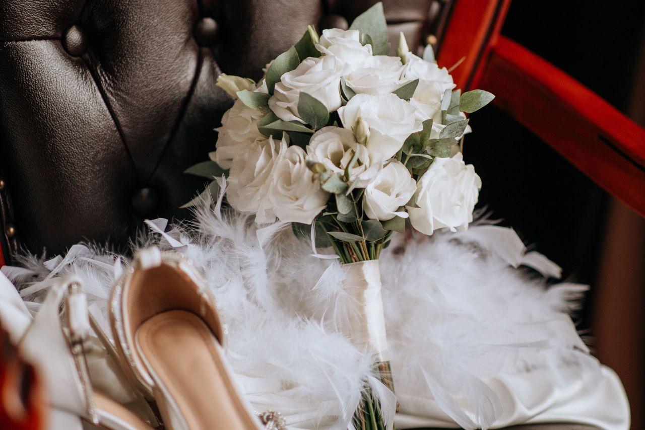 A bouquet of white roses on the black chair near the bride’s shoes.