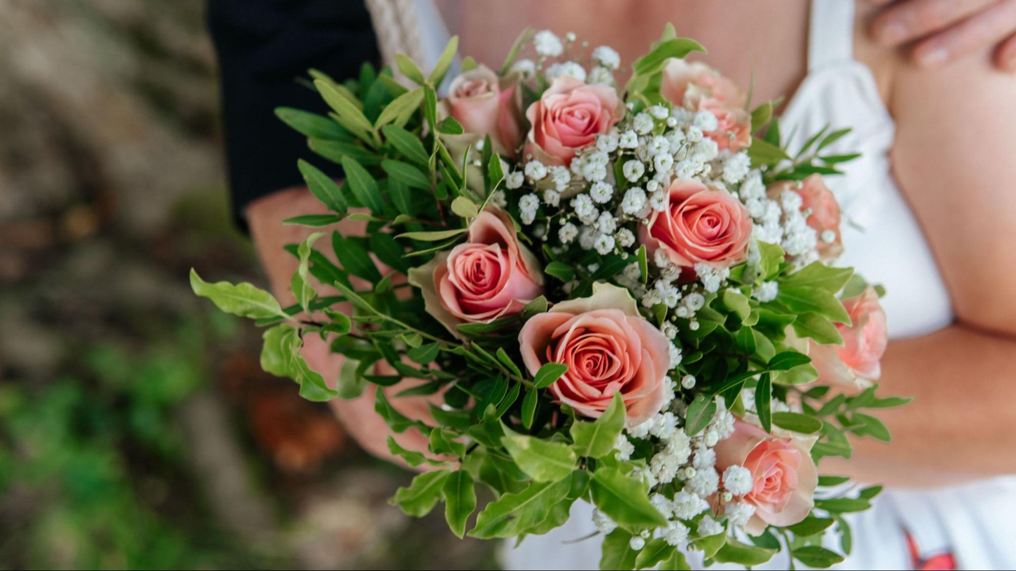 A close up of a couple holding a wedding bouquet with several pink roses.