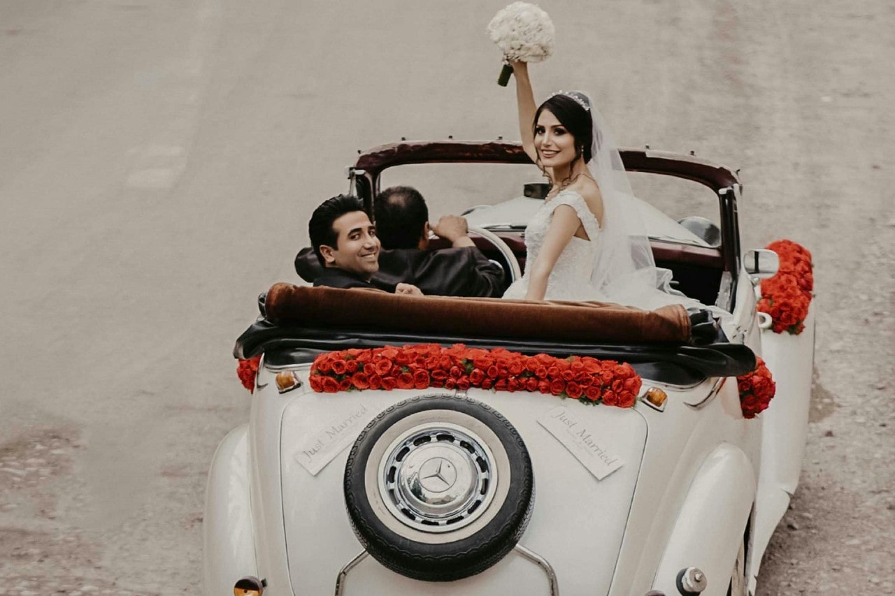 Bride and groom in a vintage car decorated with red roses.