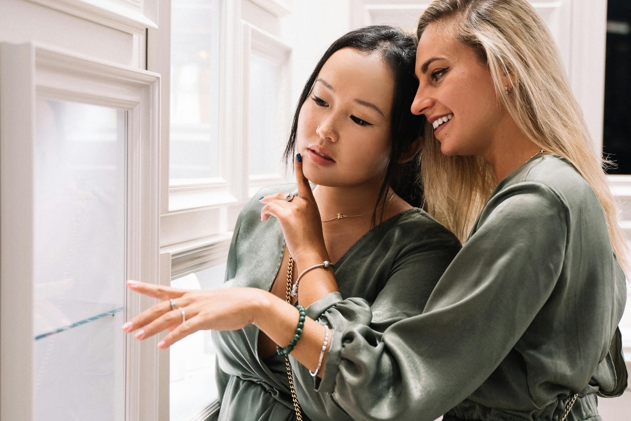 Two women twinning in olive green dresses joyfully exploring a jewelry display.