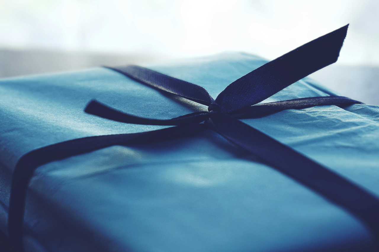 A close-up of a gift box wrapped in blue wrapping paper and tied off with a dark blue bow.