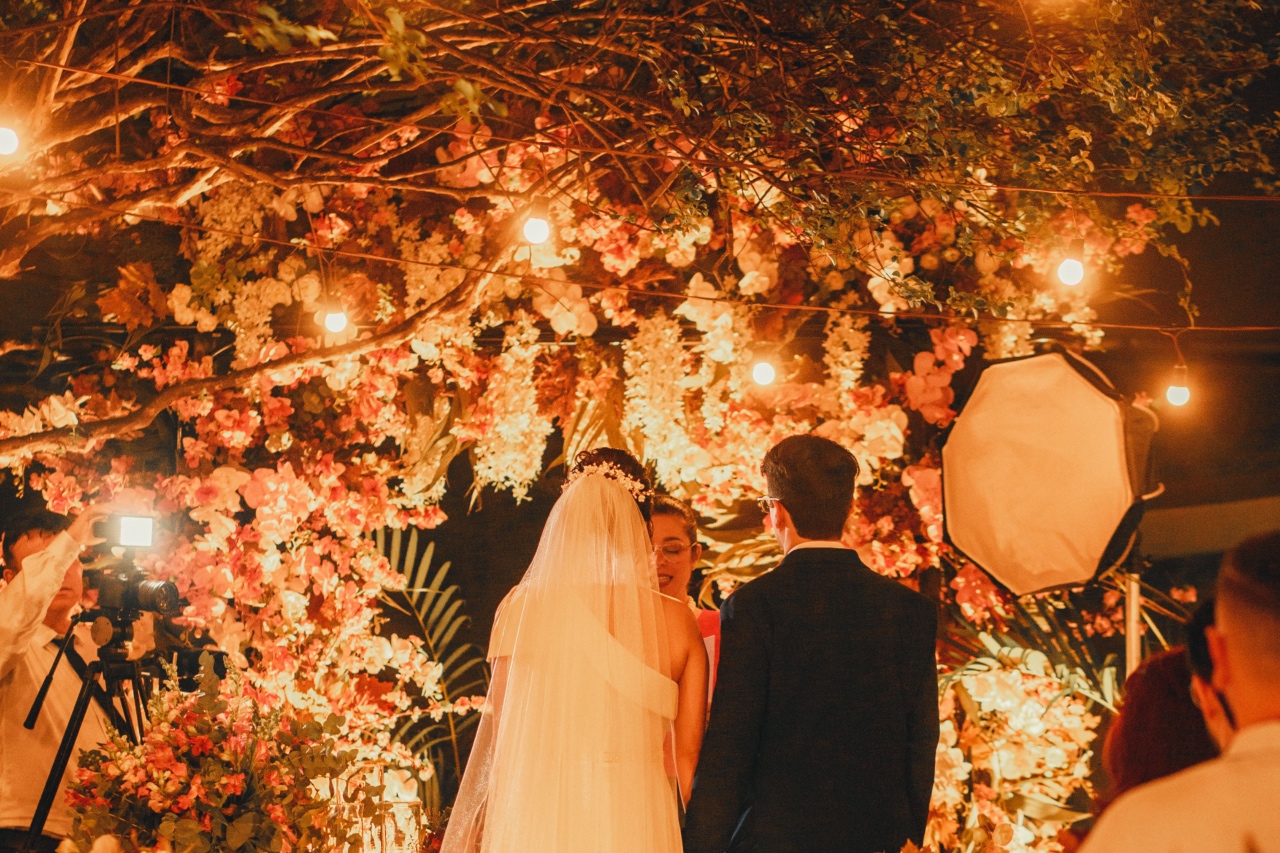 An intimate evening wedding ceremony under a canopy of trees, hanging flowers, and glowing fairy lights.