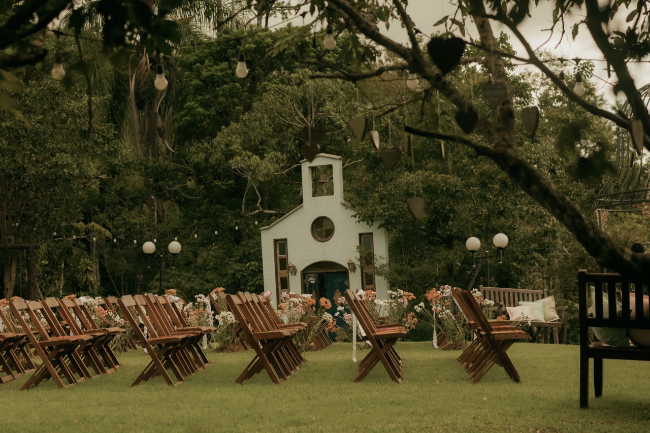 A rustic outdoor wedding ceremony set up on a green lawn with a small chapel in the background.