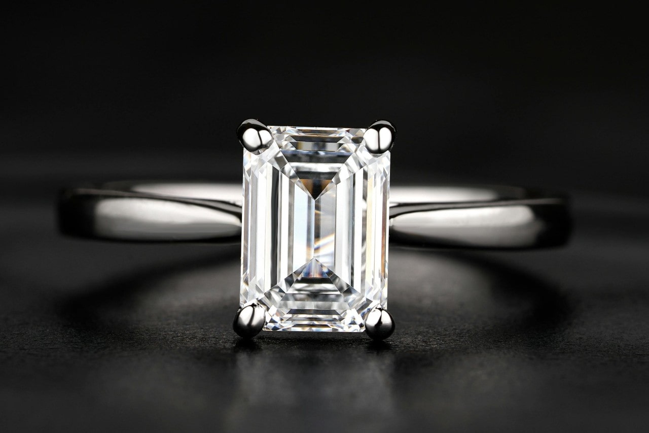A close-up of a stunning sapphire cut solitaire engagement ring on a dark background.
