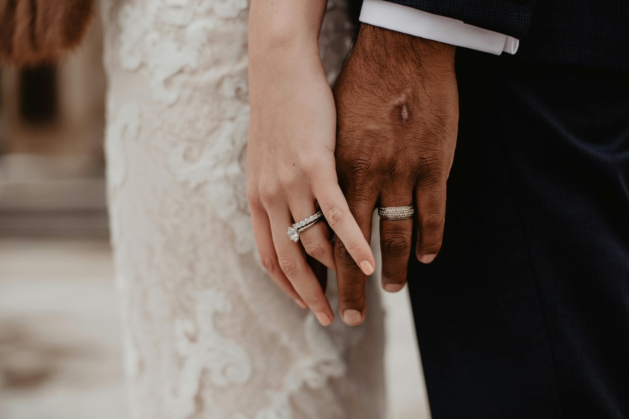A bride and groom holding hands with a focus on the groom’s wedding band and the bride’s wedding band and engagement ring.