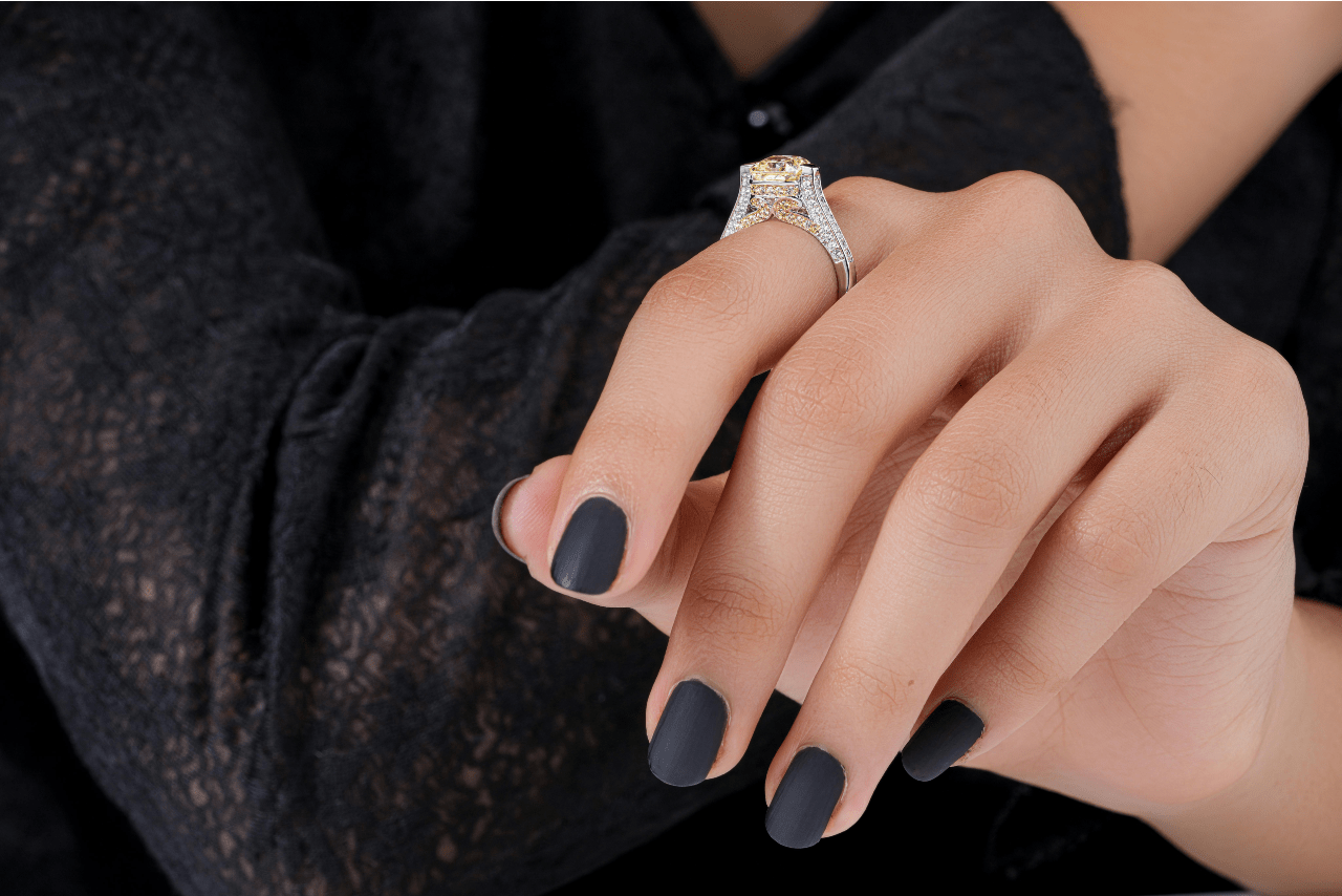 A close-up of a woman’s manicured hand, a distinctive engagement ring on her finger.
