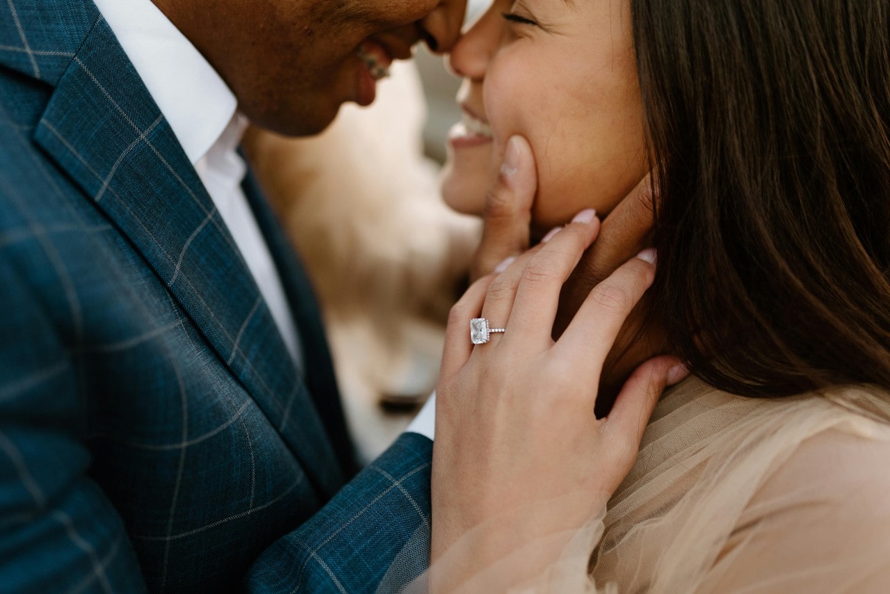 A close-up of an engaged couple in a loving embrace, with emphasis on the bride-to-be’s elegant engagement ring.