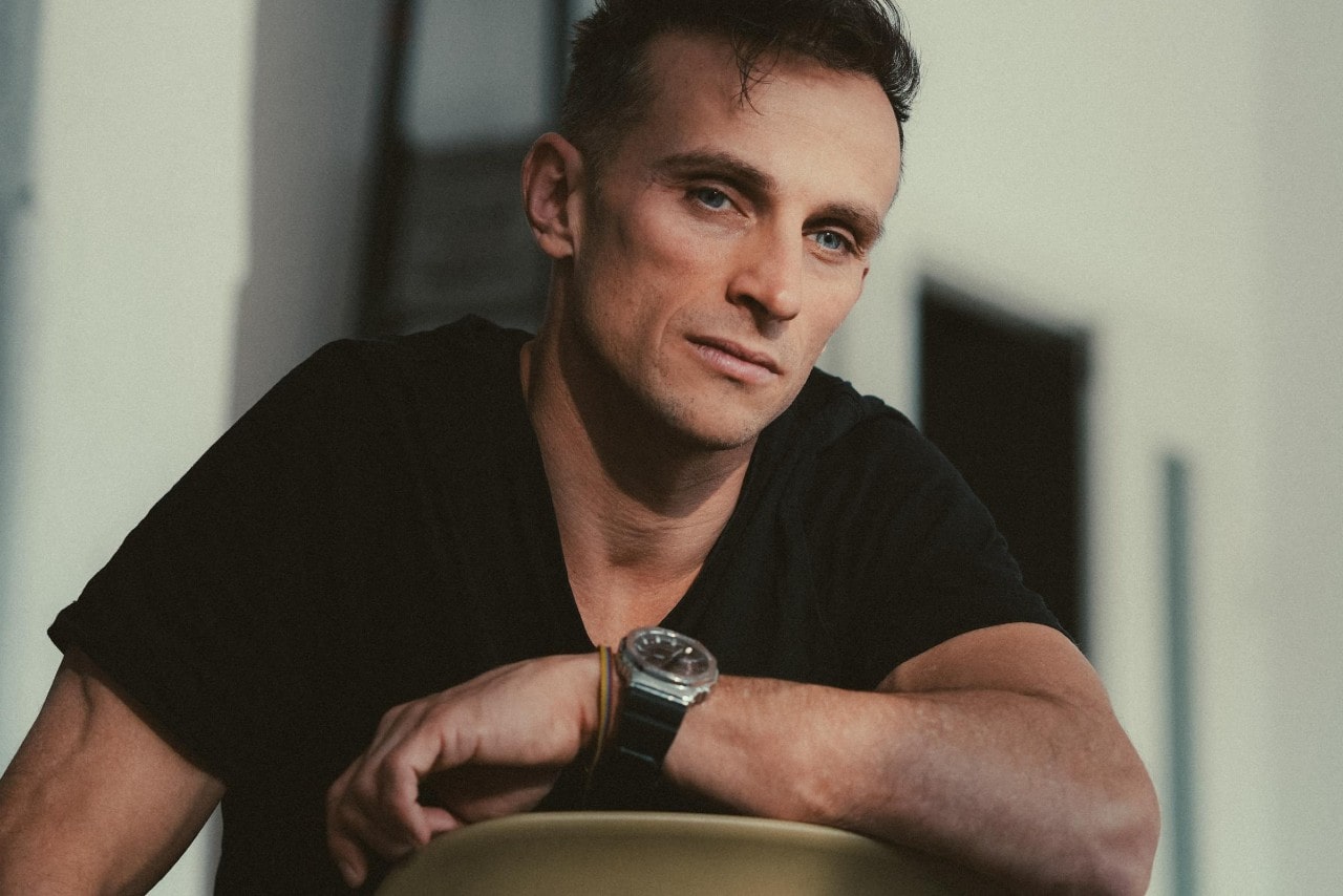A man sitting backwards in a chair wearing a black shirt and black watch.