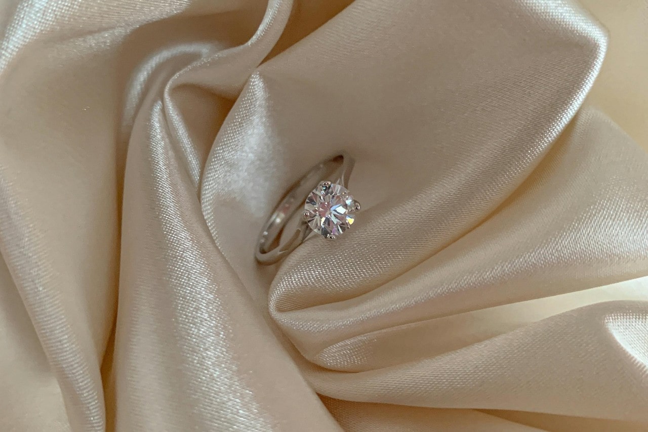 a diamond solitaire engagement ring sitting on a piece of cream fabric