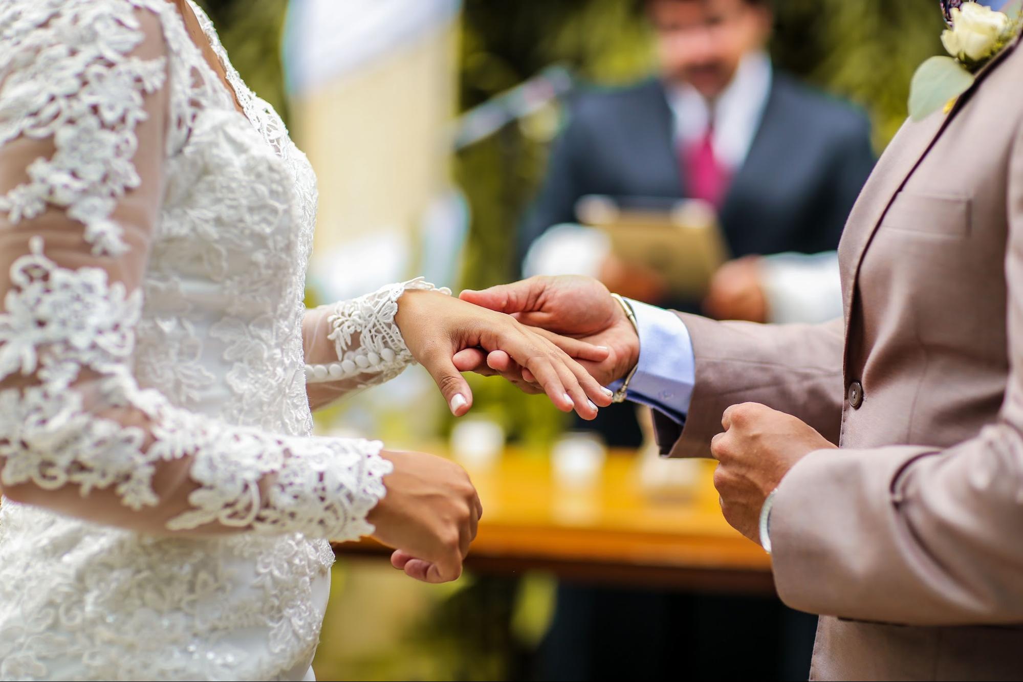 A close-up of a groom placing a wedding ring on the bride's finger during an outdoor ceremony.