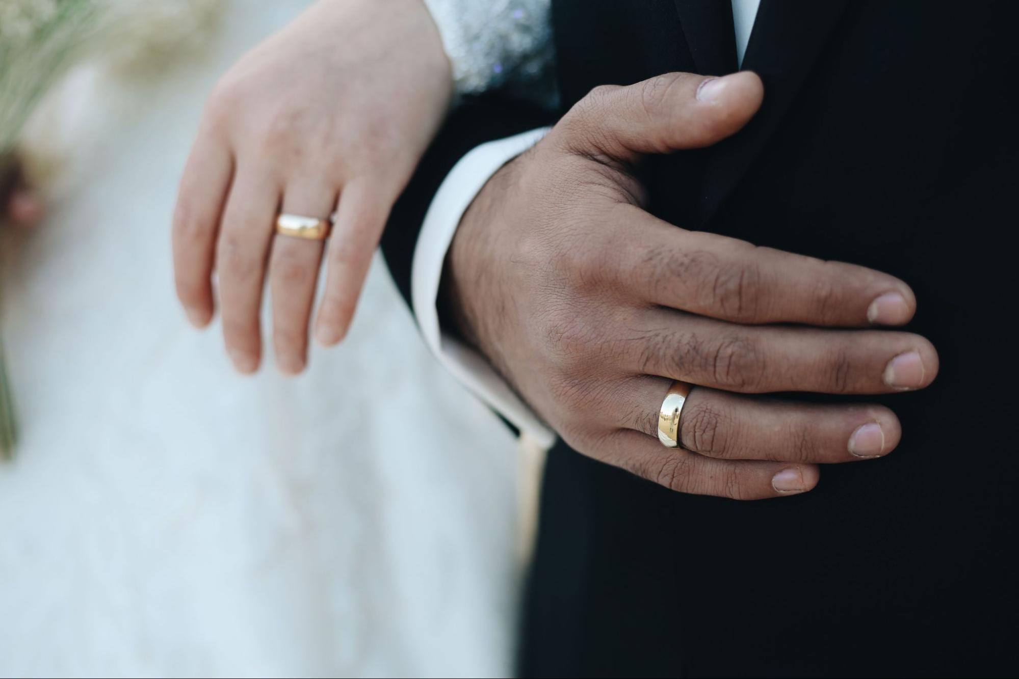 A close-up of a newlywed couple’s hands with matching yellow gold wedding bands.