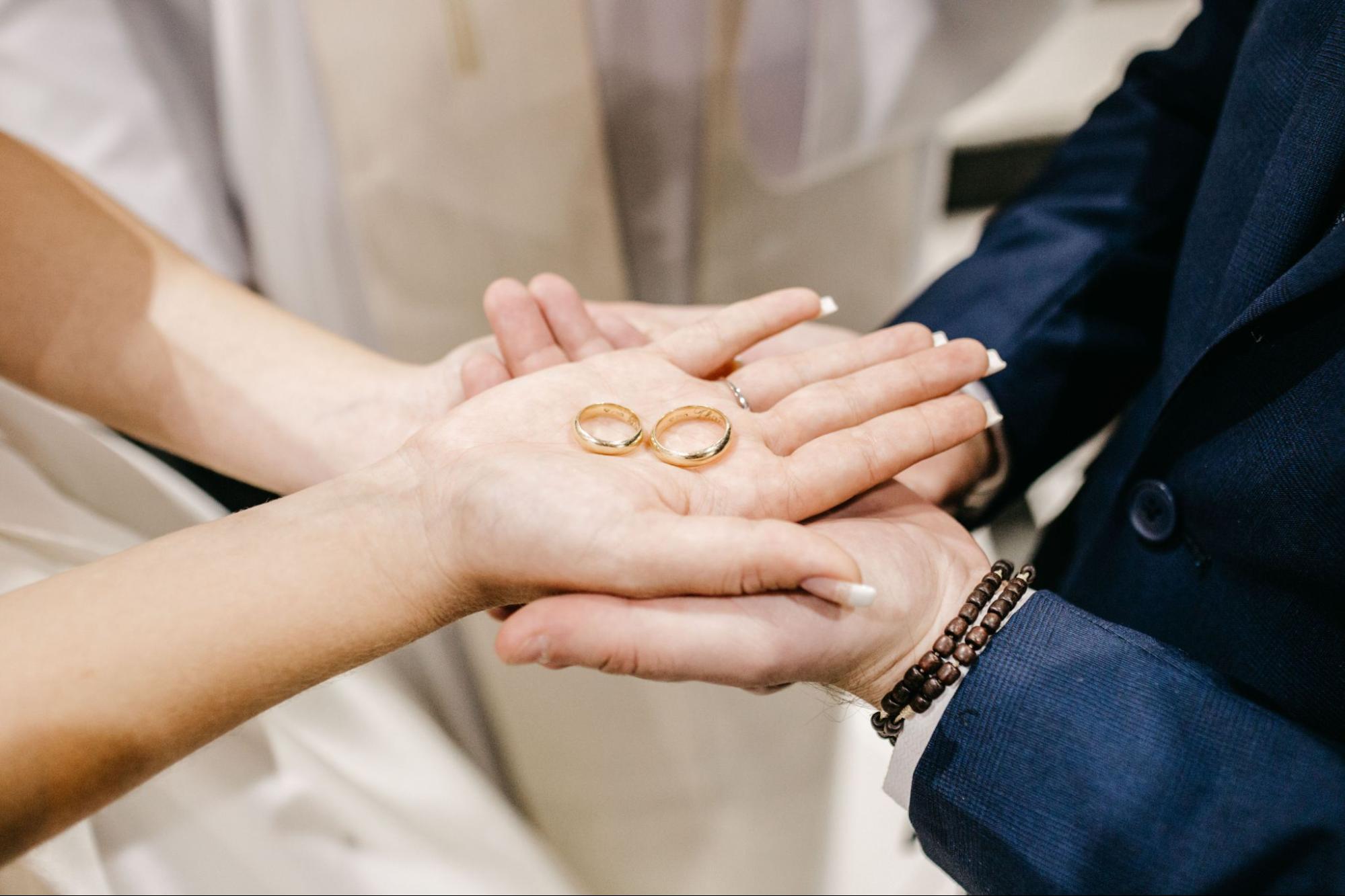 A newlywed couple holding palms together, showcasing a matching yellow gold wedding band set.