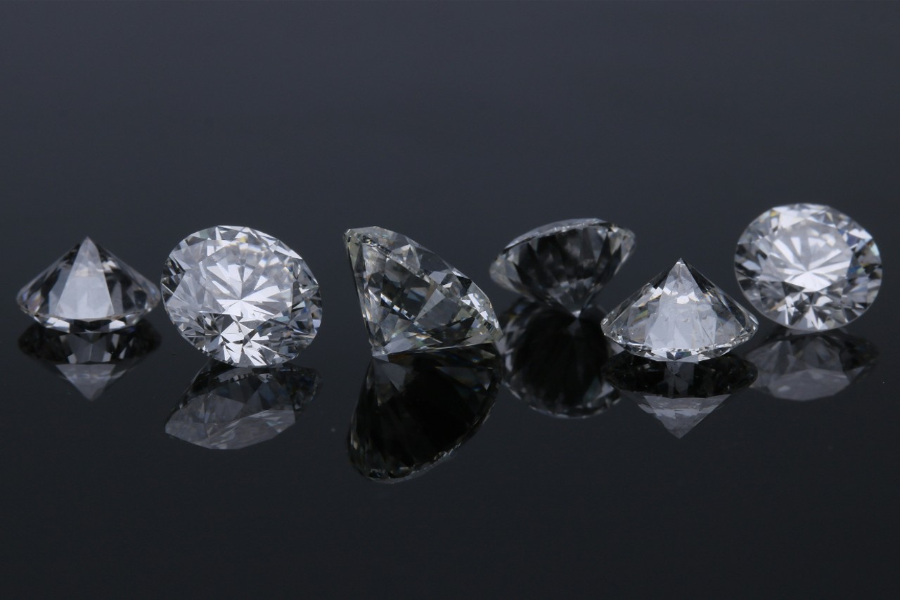 six round cut diamonds sitting in a line on a black reflective surface