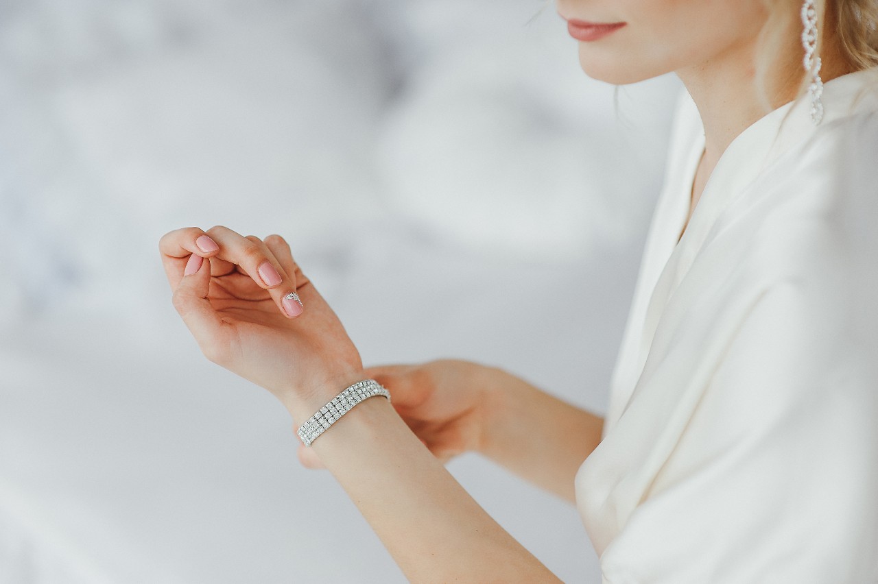 A woman adorned in diamonds fastens a tennis bracelet around her wrist.