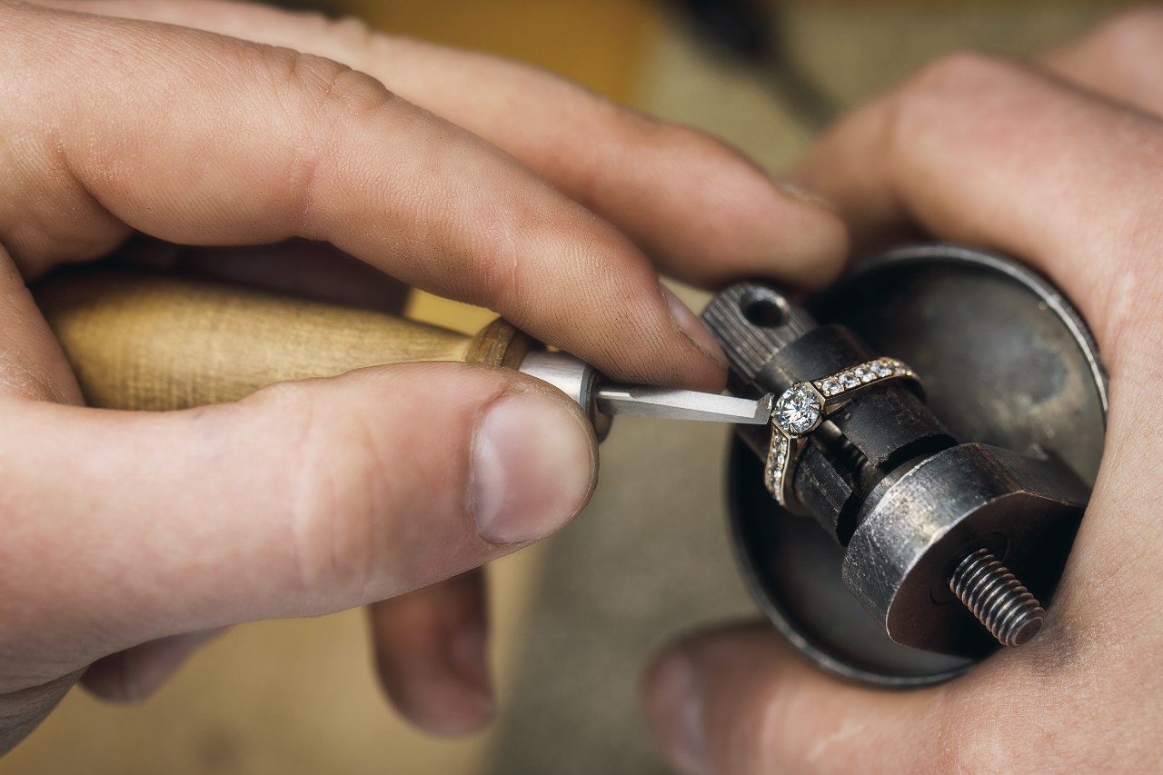 A jeweler adjusts the prongs on a yellow gold diamond ring.