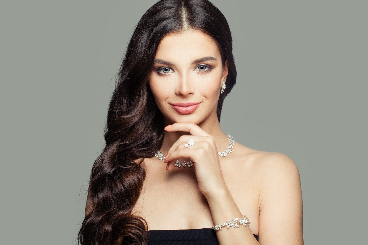 a model wearing an array of diamond jewelry in front of a gray background.