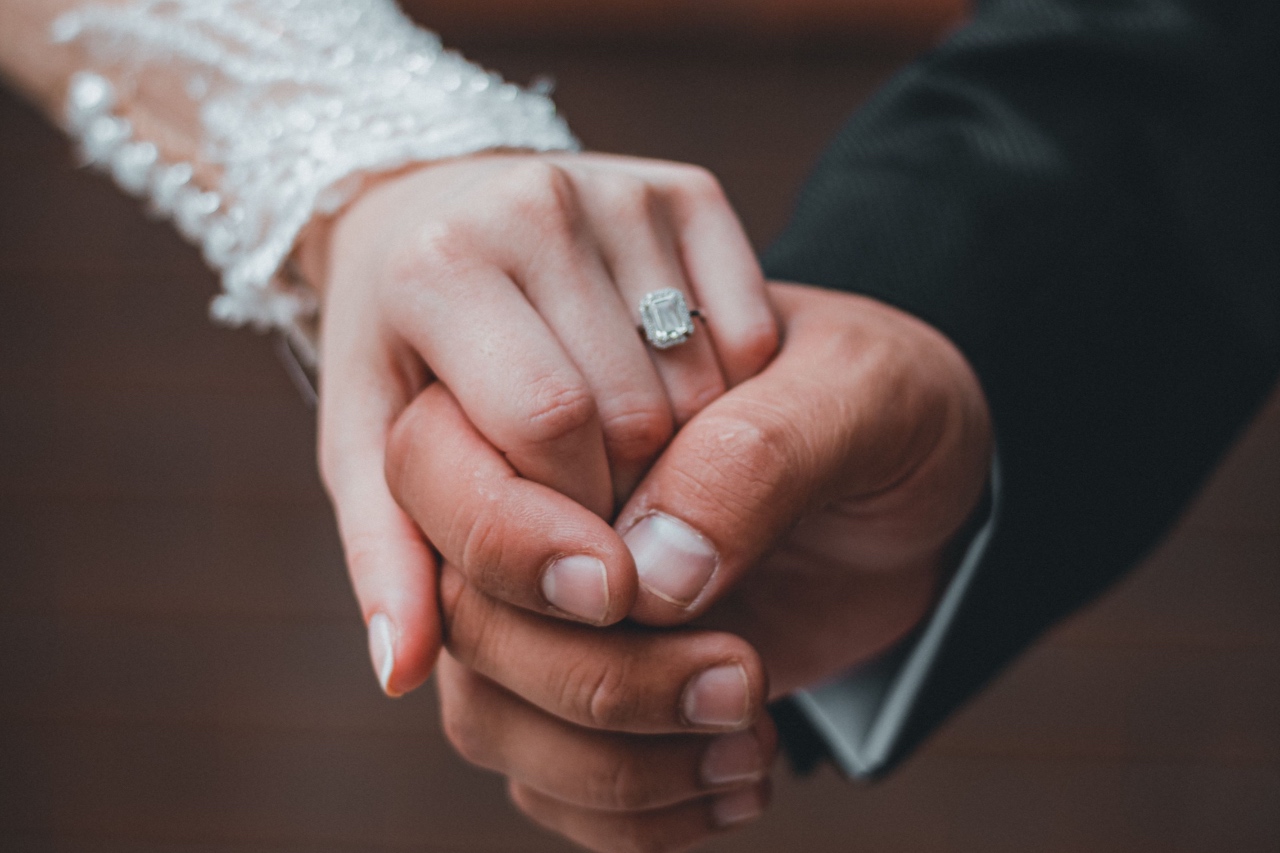 A bride and groom holding hands in their wedding attire, showcasing the bride’s engagement ring.