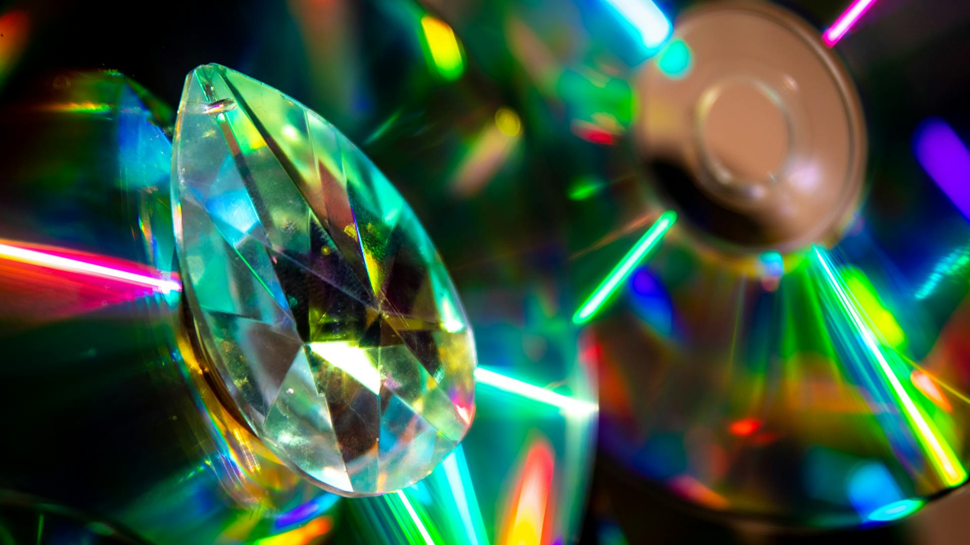 A close-up of a pear cut diamond displayed between two illuminated CDs.
