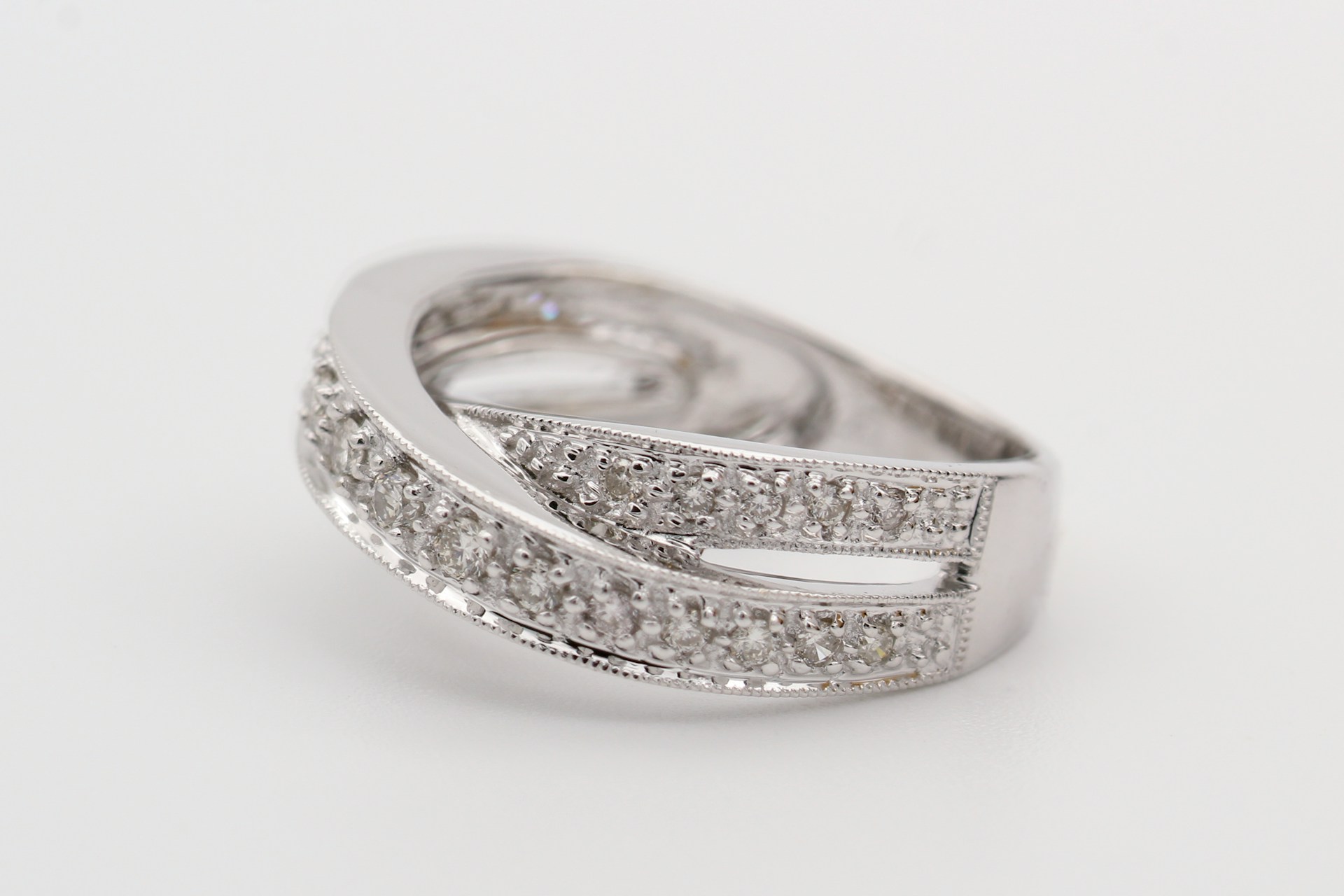 A close-up of a white gold split shank band with pavé-set round diamonds on a white backdrop.