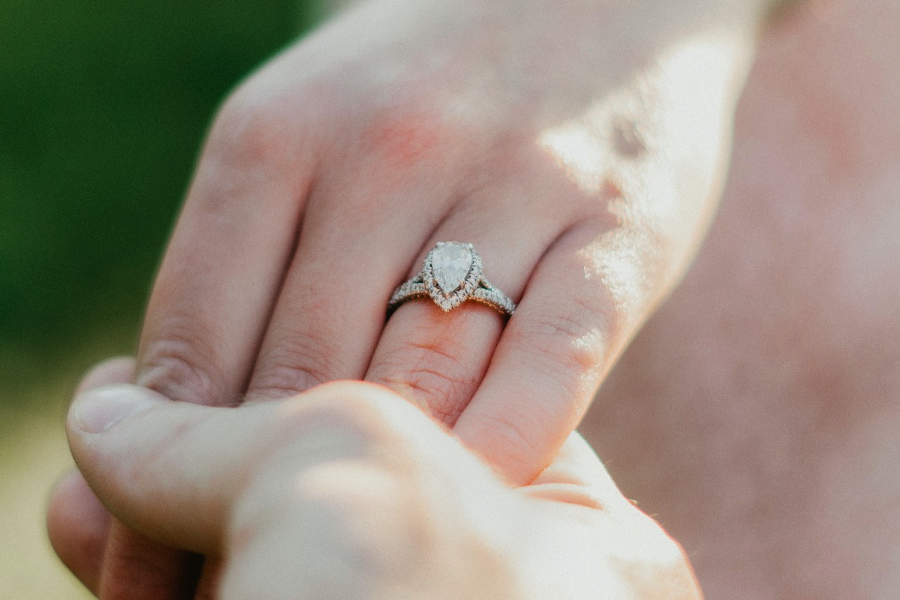 a man’s hand holding a woman’s hand wearing a pear shape engagement ring with a split shank