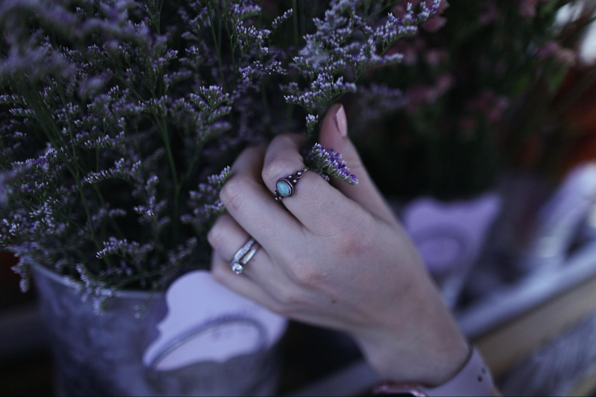 A woman grabs a lavender flower wearing her bridal jewelry and a turquoise fashion ring.