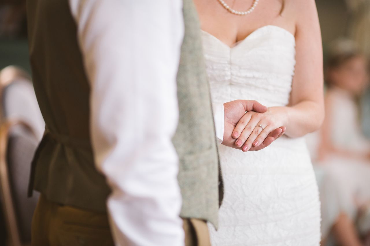 a bride and groom holds hands, showing off her wedding band.