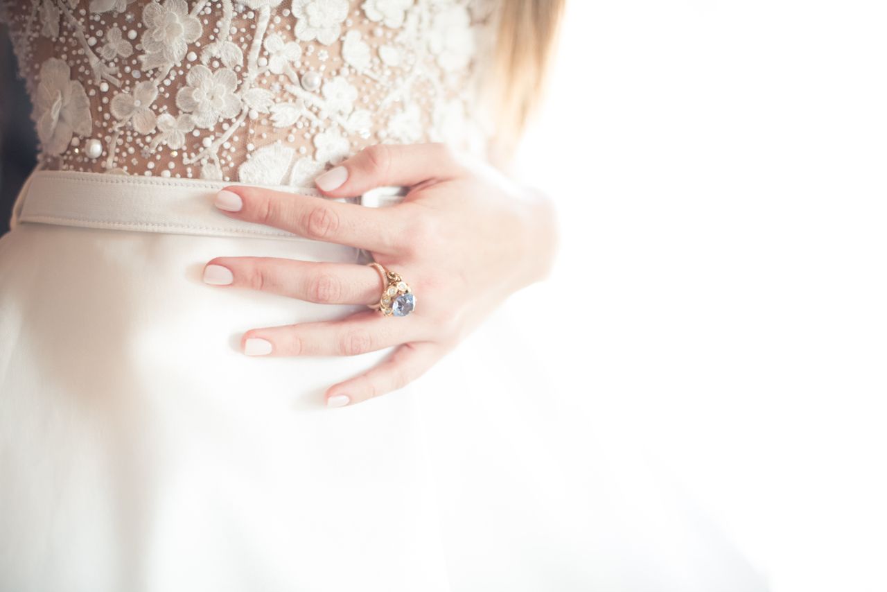 A bride standing by a window wears a blue topaz engagement ring.