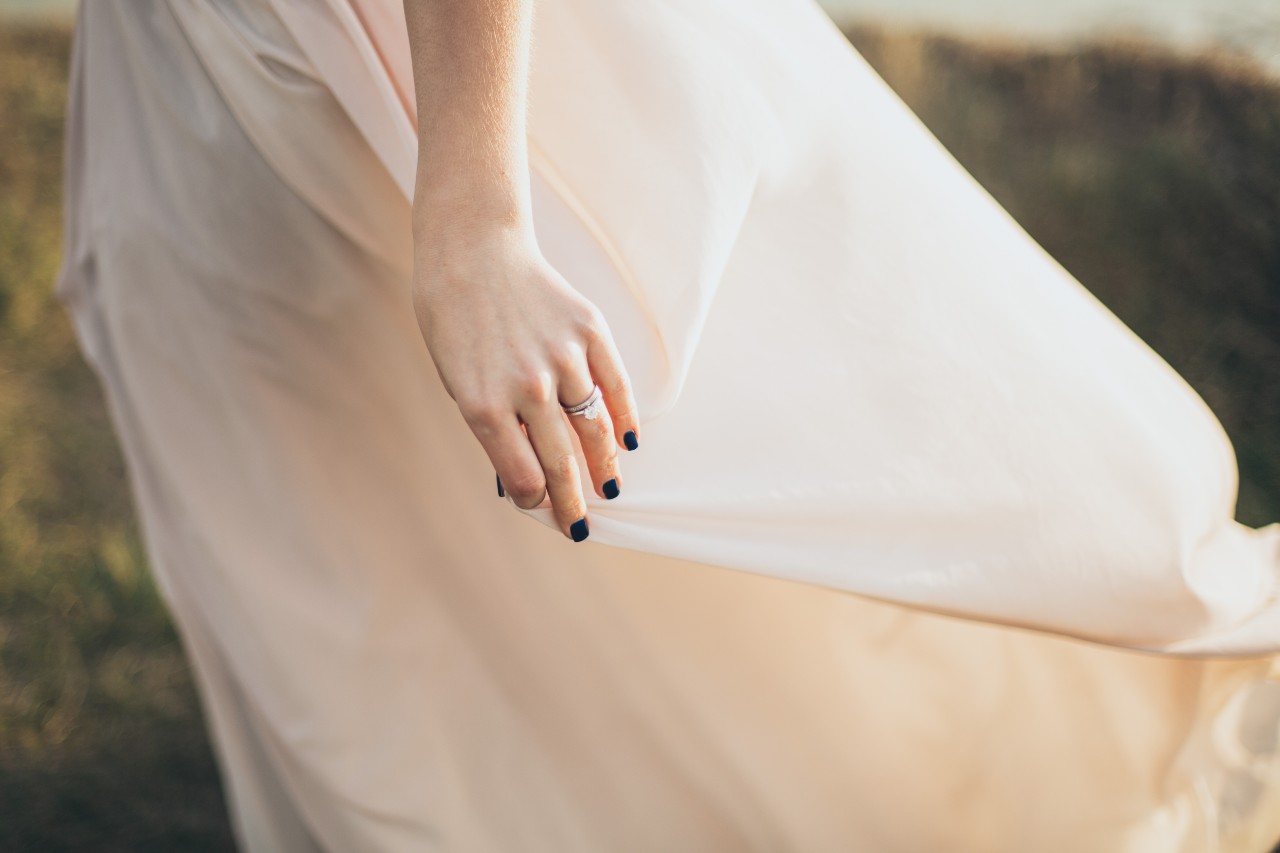 a woman grabs her gown’s skirt as the wind blows, showing off her bridal jewelry.