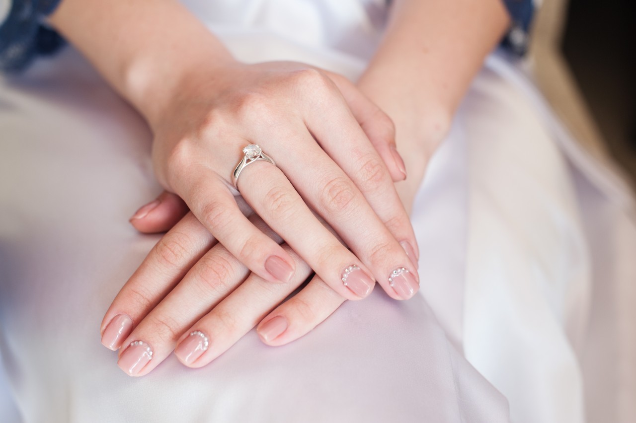 a bride with manicured nails rests her hands on her satin wedding dress.