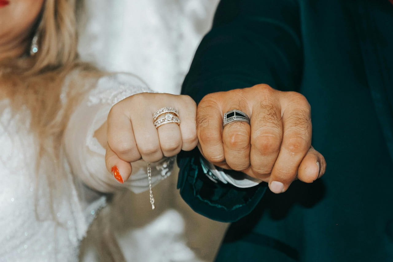 A close up of a newlywed couple holding their fists together, showcasing their wedding bands.