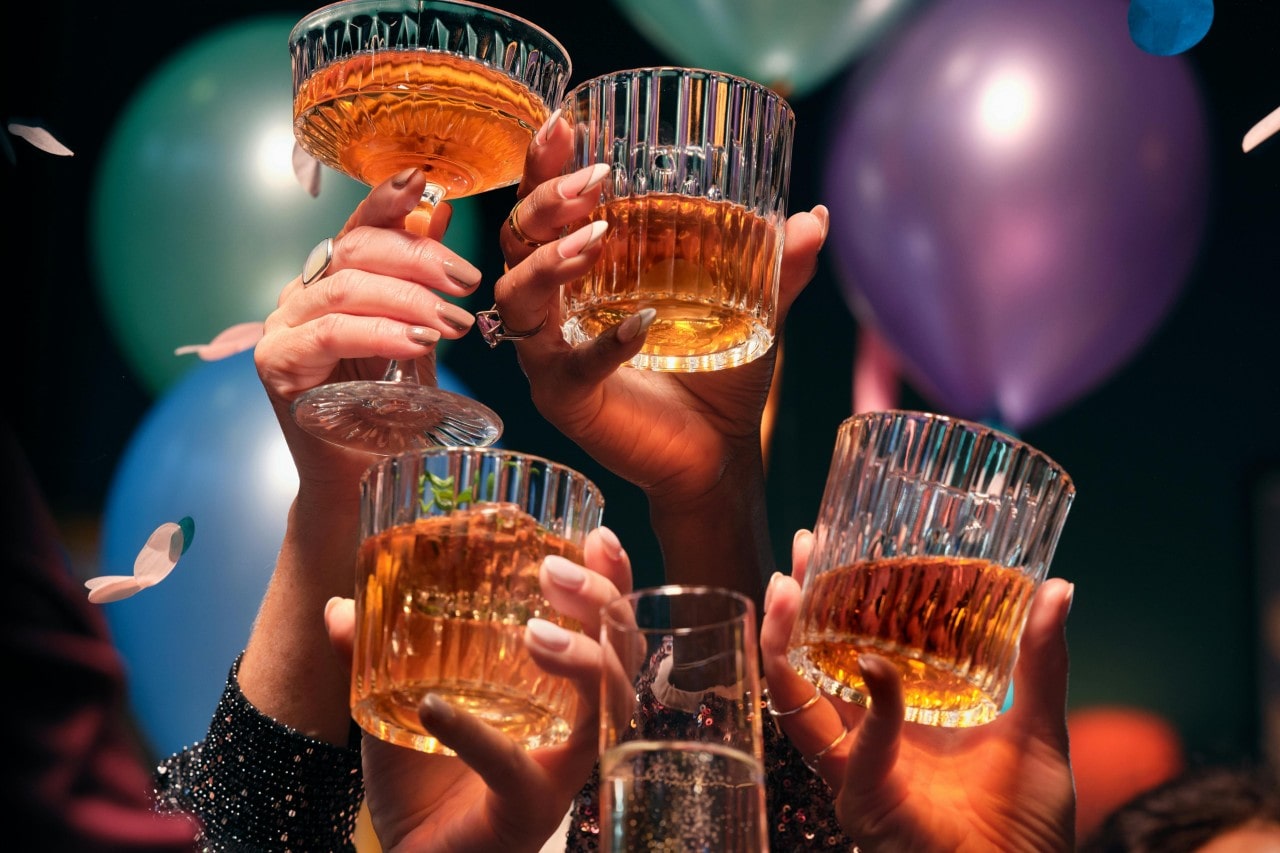 Several hands with glasses filled with whisky held together celebrating something