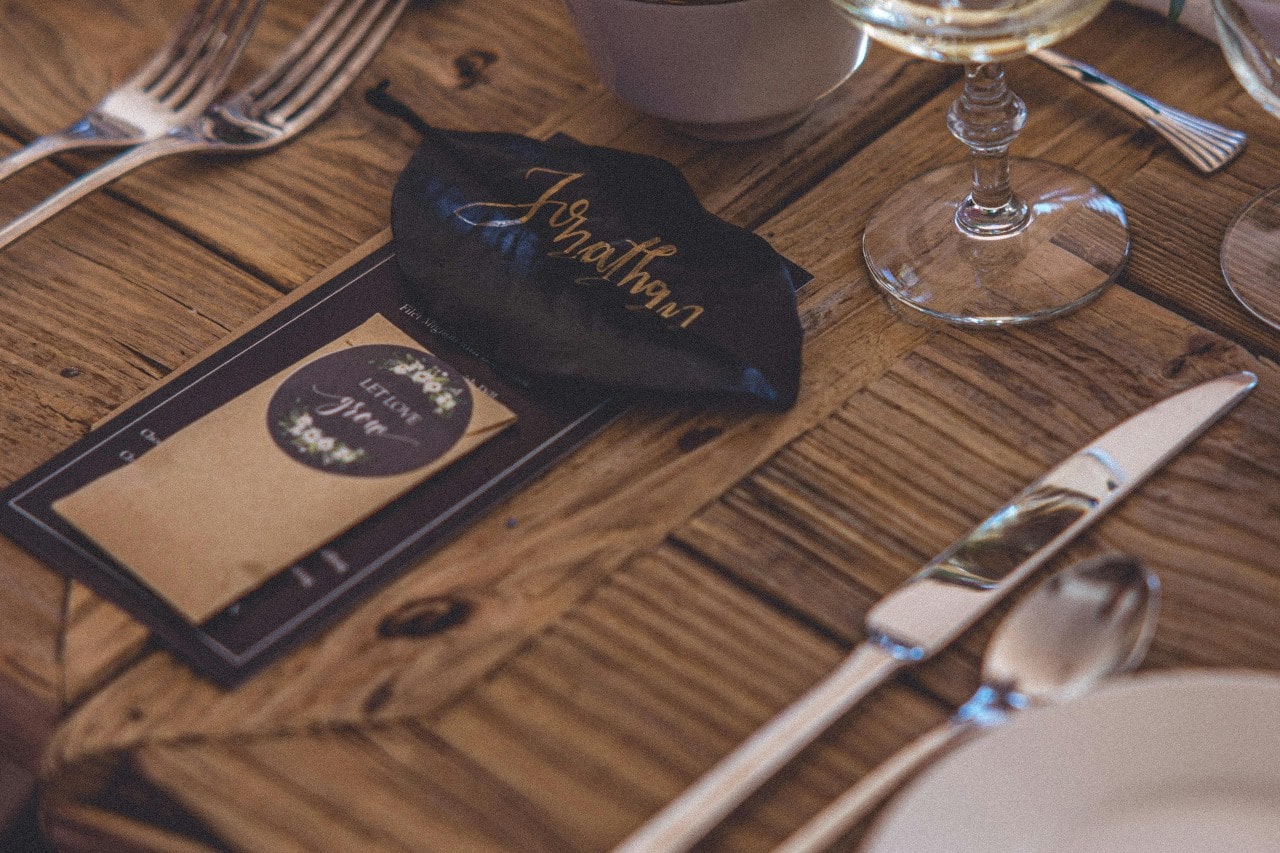 A close up of a wooden table with a wedding card and a name of a guest on it
