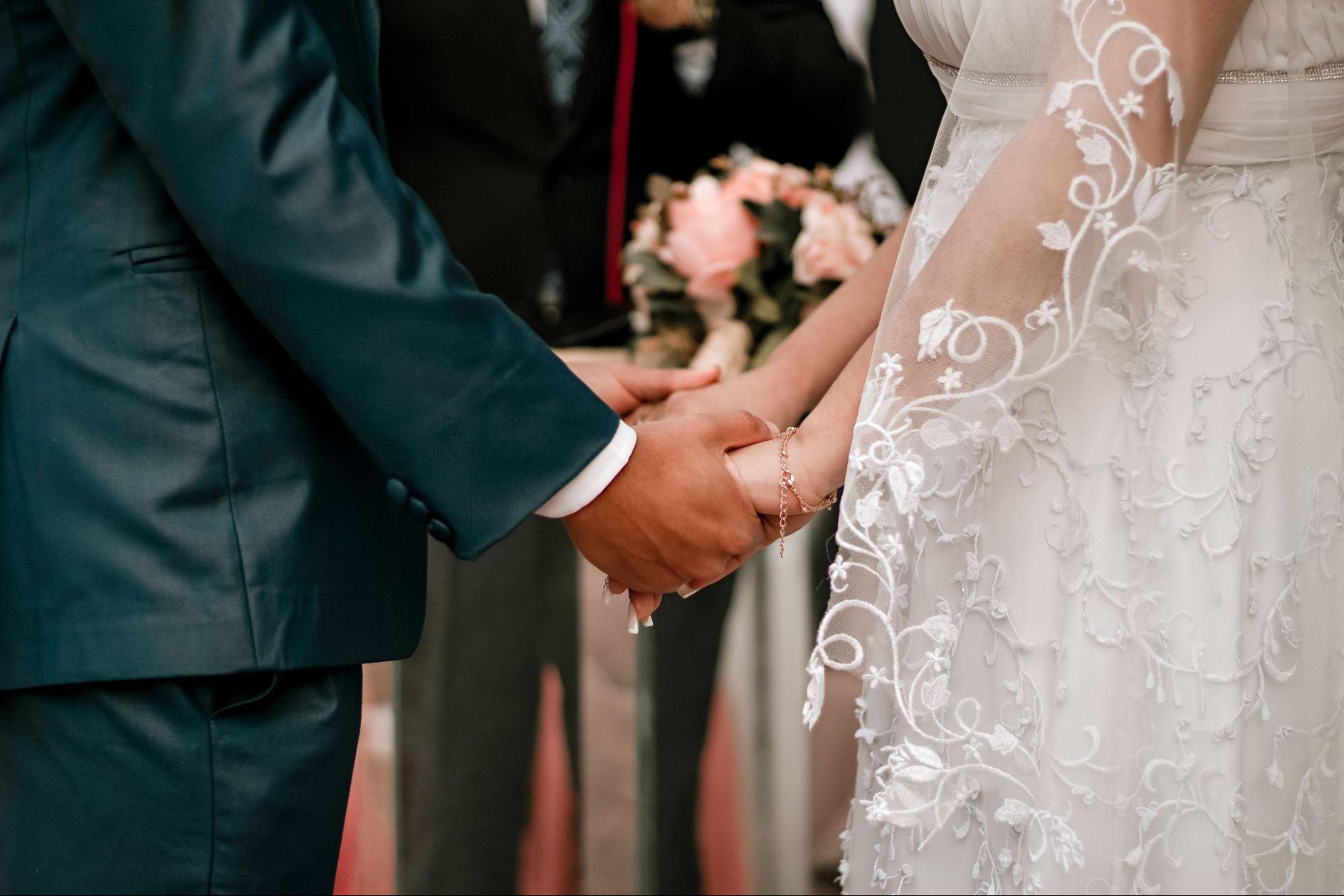 A close up of a bride and groom holding hands at the altar.
