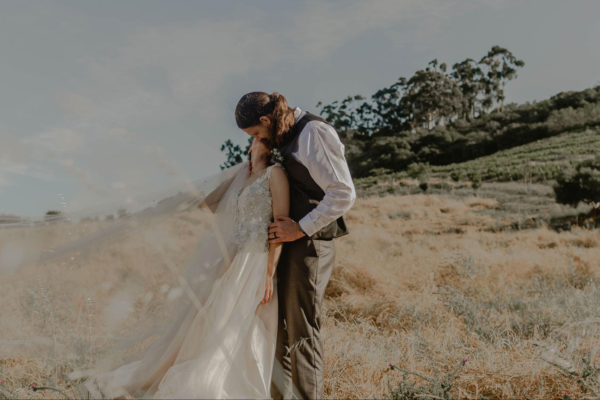 A newlywed couple kiss while standing in the middle of the field.