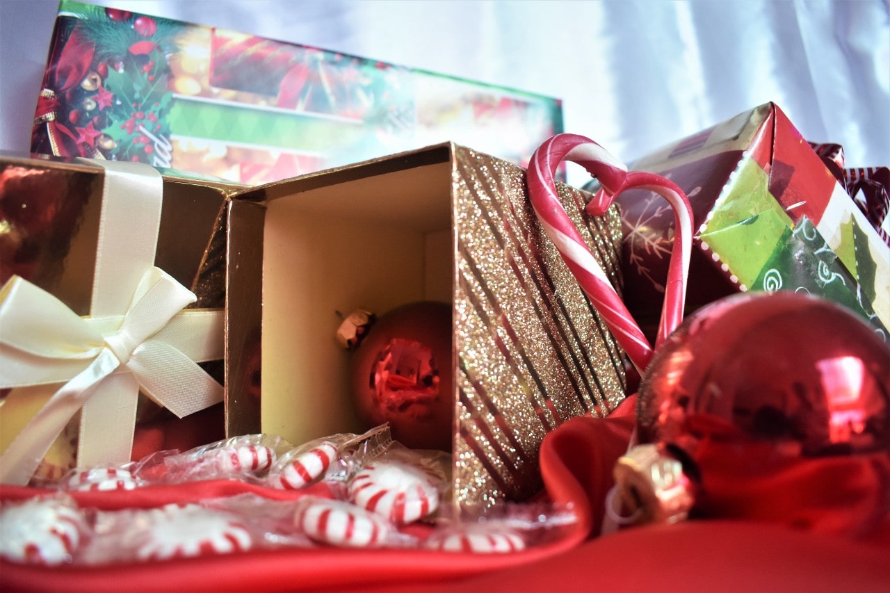 A festive arrangement of Christmas gifts, candy canes, red ornaments, and peppermint candies displayed with glittery and colorful wrapping.