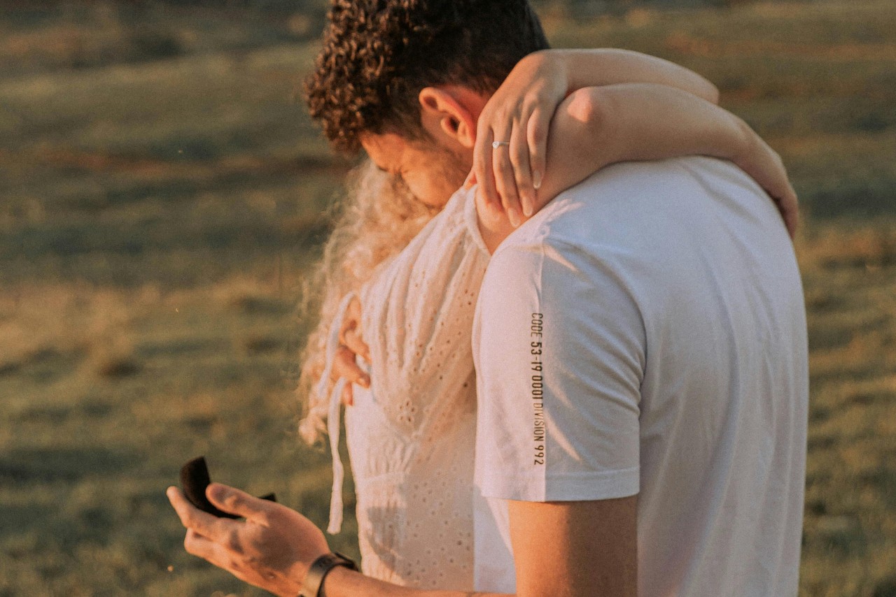 a couple embracing in a field, the man holding a black ring box
