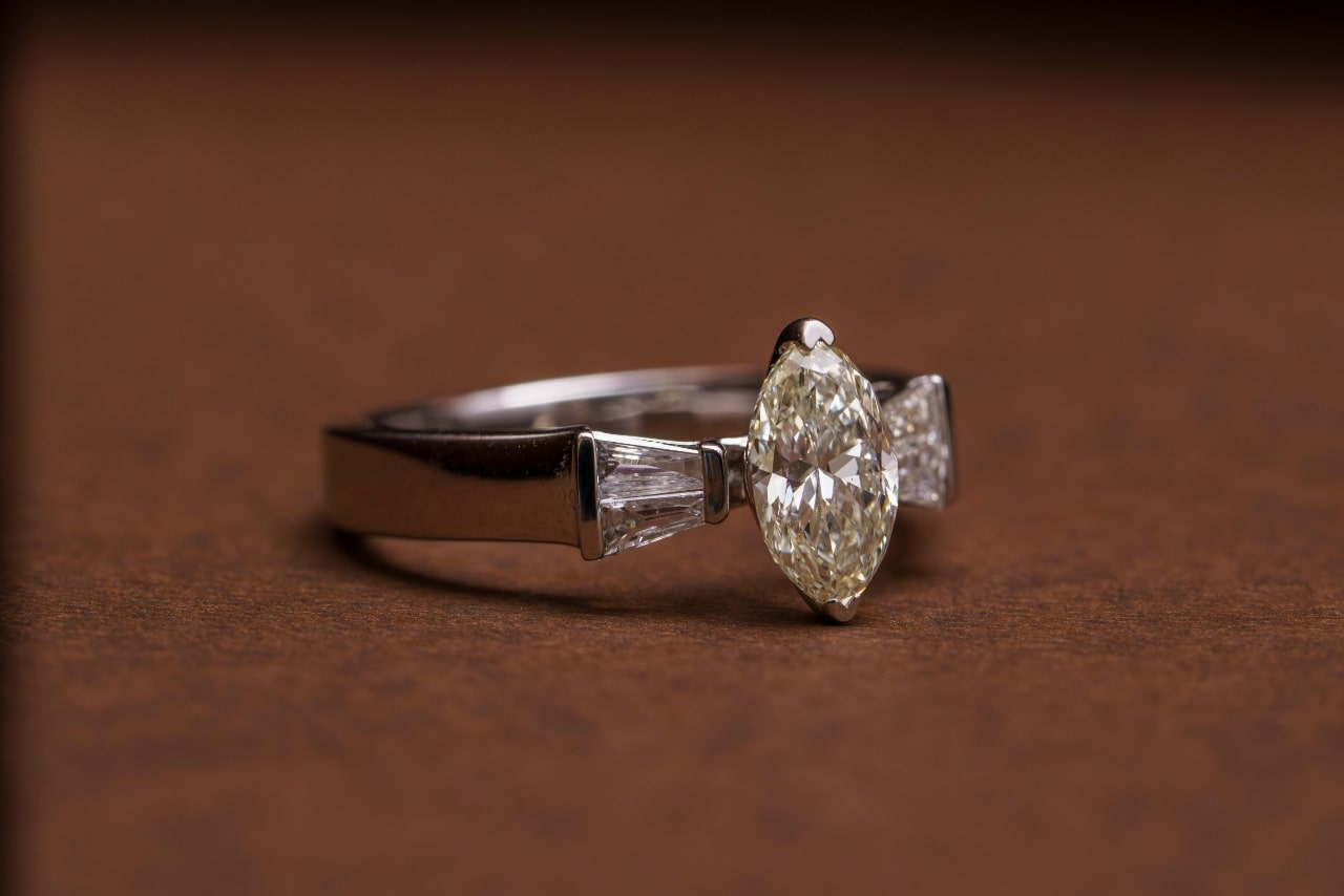 A close up of a three stone white gold engagement ring with a marquise cut diamond center stone.