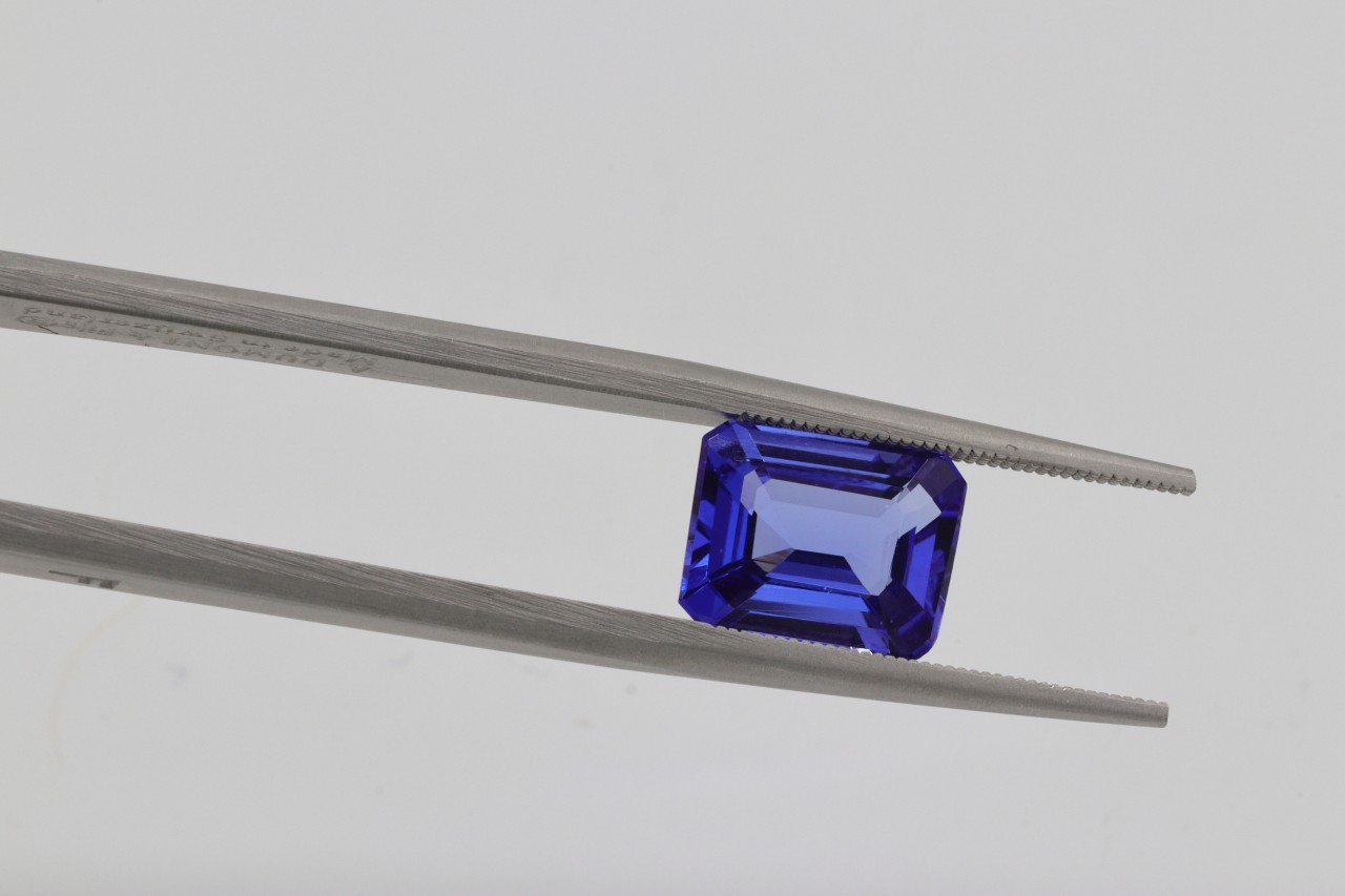 a pair of tweezers holding an emerald cut blue gemstone