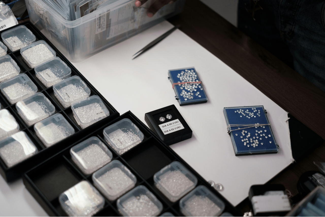 A view of diamonds of different sizes sorted into clear containers on a desk with tweezers.