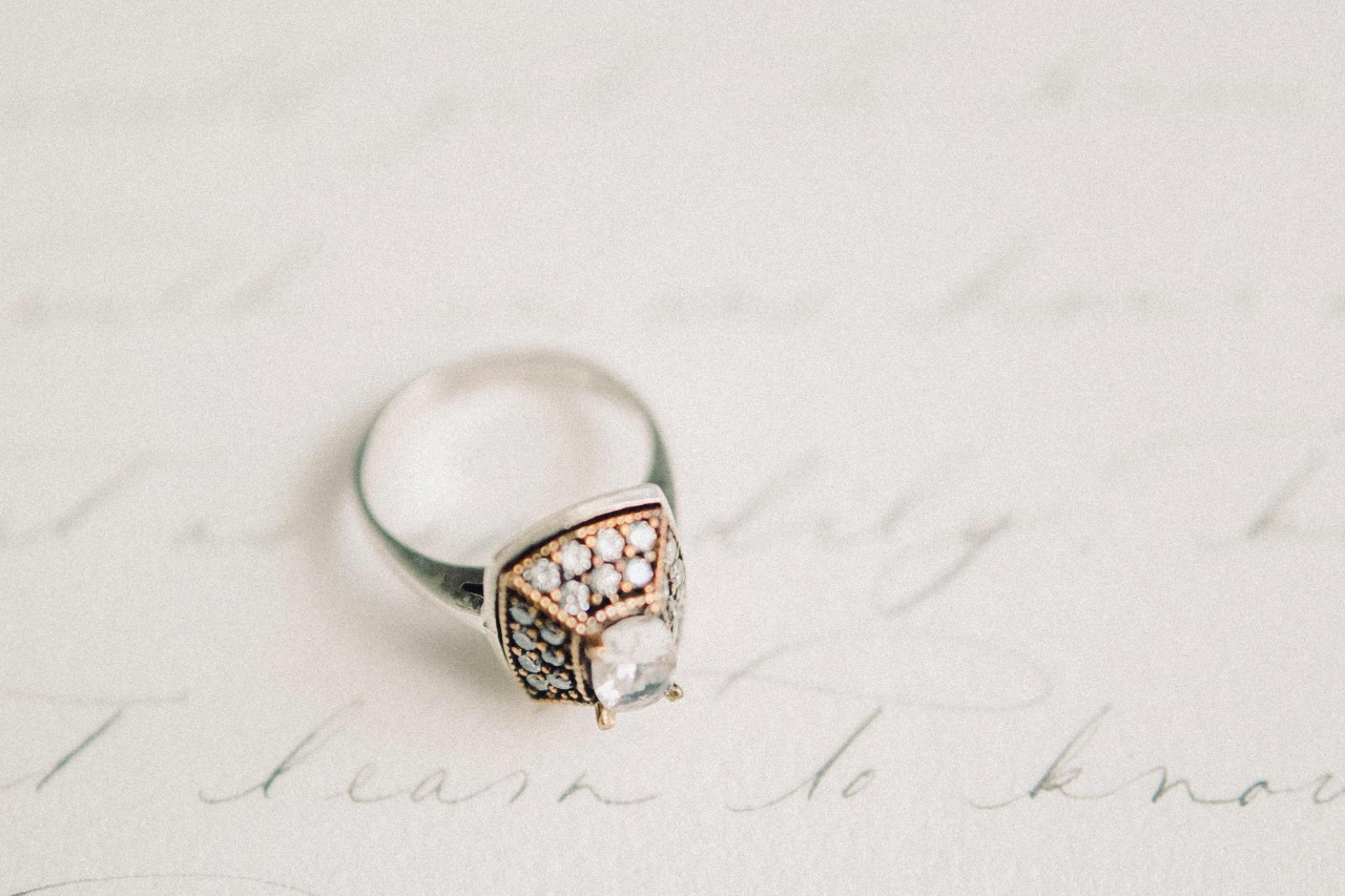 A close-up of an opulent engagement ring atop hand-written wedding vows.