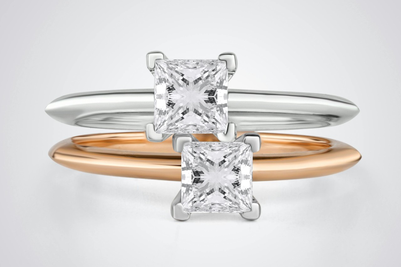 two princess cut solitaire engagement rings in different metals stacked on top of each other
