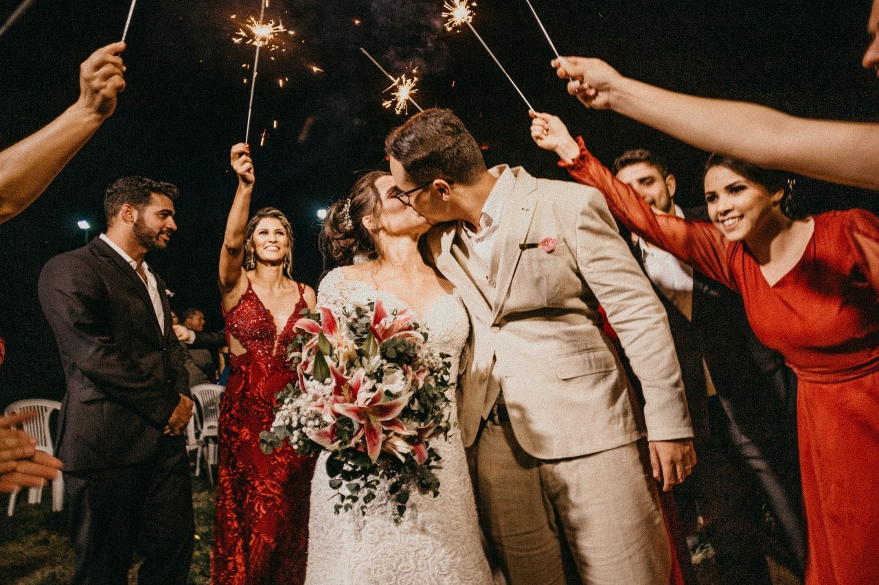 a bride and groom embracing under an arch of sparklers held by their wedding party